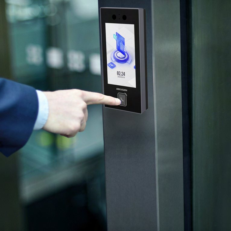 Persona usando un terminal de acceso biométrico con pantalla táctil junto a una puerta de vidrio